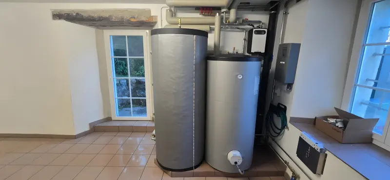 Chaufferie d'une maison de maître à Loveresse après la pose de la pompe à chaleur, accumulateur et chauffe-eau alignés sur un sol net
