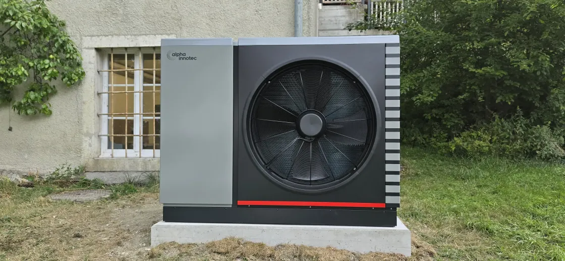 Pompe à chaleur alpha innotec Hybrox 21 sur son socle en béton devant la façade en pierre d'une maison de maître des années 1900, chantier de Loveresse