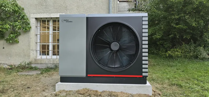 Pompe à chaleur alpha innotec Hybrox 21 sur son socle en béton devant la façade en pierre d'une maison de maître des années 1900, chantier de Loveresse