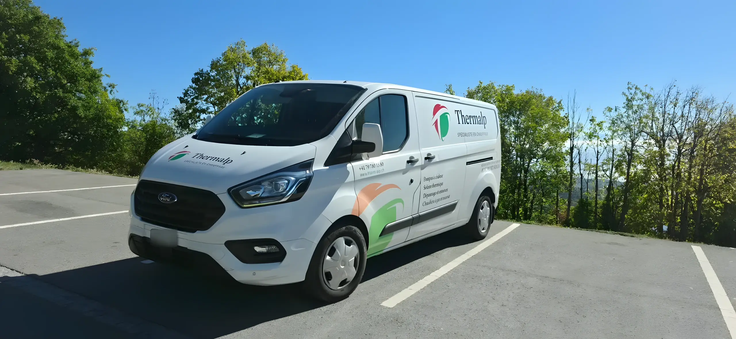 Fourgon d'intervention Thermalp, floqué aux couleurs de l'entreprise, sur un parking bordé d'arbres